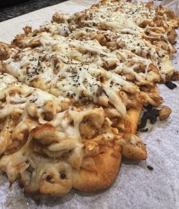 A picture of a piece of flat bread baked and topped with buffalo sauce, melted mozzarella (white cheese), diced chicken breast, mushrooms and onions.